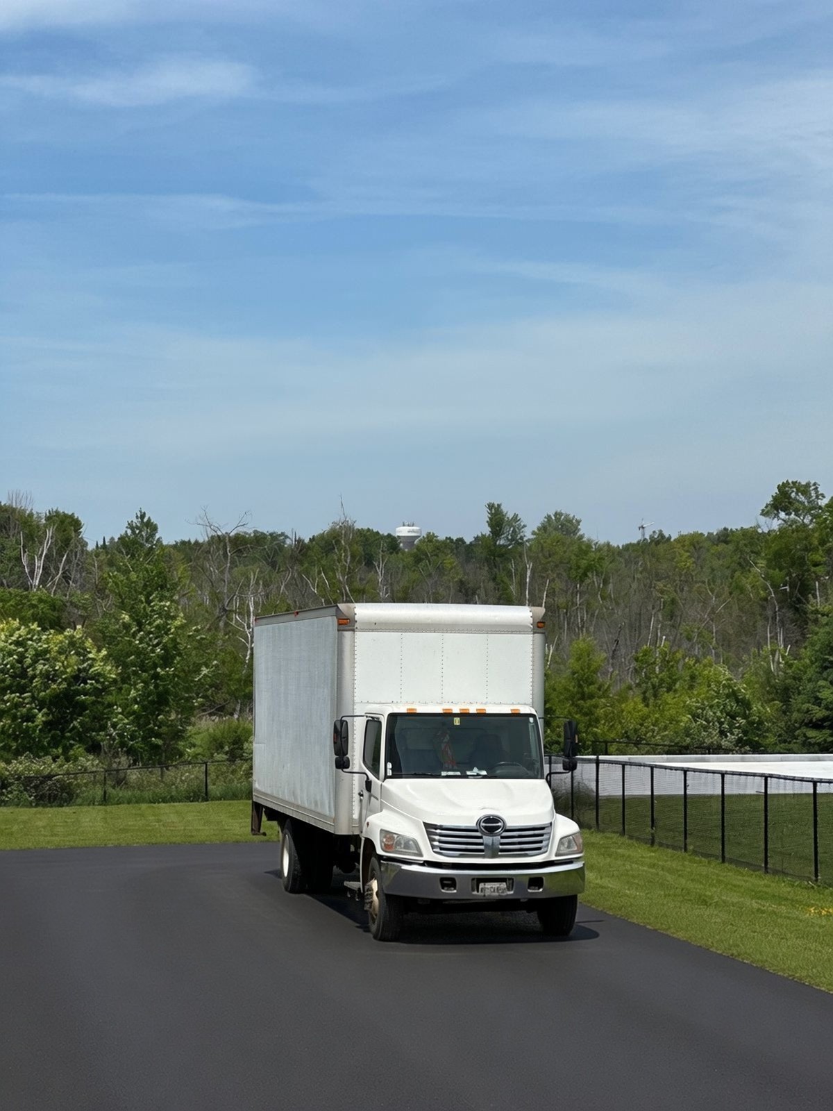 White Hino straight box truck parked on fresh pavement, with trees behind it.