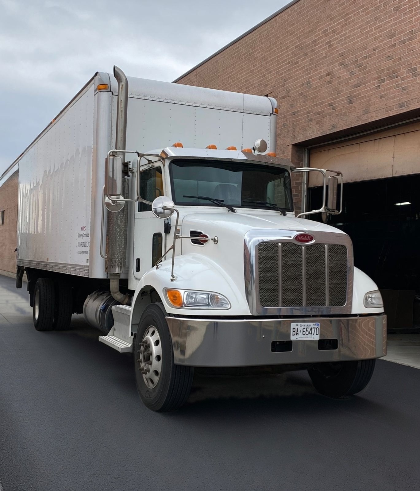 White Peterbilt straight box truck lettered KVRS Delivery Services, parked at a brick industrial building.